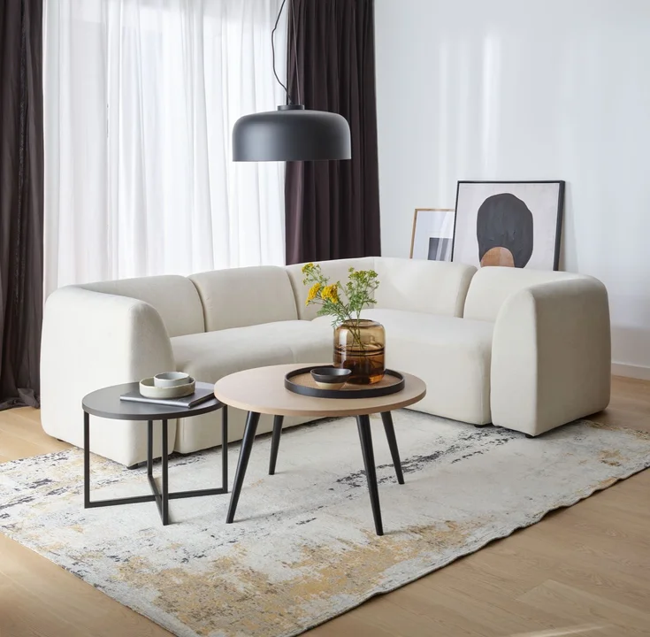 Elegancki salon z jasną sofą i dużą czarną lampą wiszącą nad stolikami kawowymi.